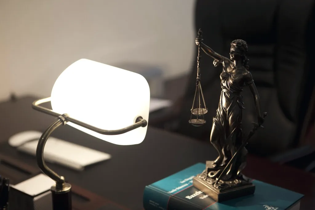 Statueta Justiției cu balanța, lângă lampa aprinsă, pe biroul avocatului